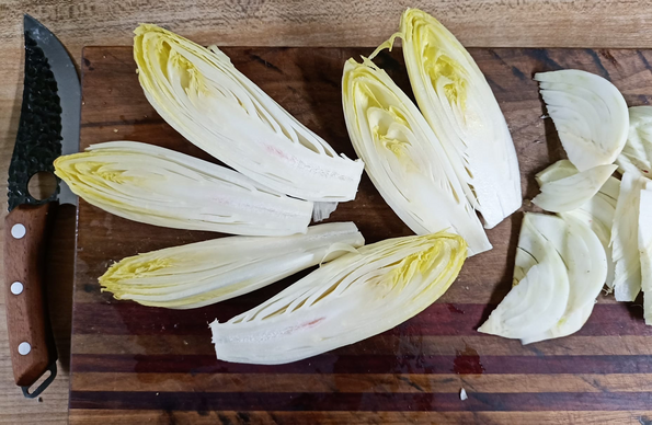 3 längs halbierte Chicorée und der geschnittene Fenchel auf einem Brett, neben dem Brett liegt ein Handliches Messer mit einer breiten, geschwungenen Klinge.