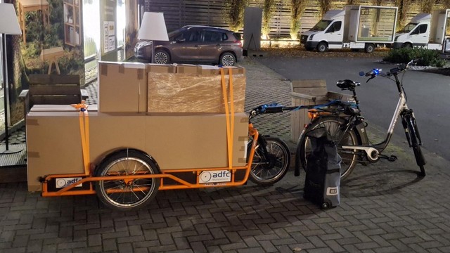 Auf dem CarlaCargo Lastenanhänger des ADFC-Münsterland sind mehrere Kartons aufgeladen, in denen die Einzelteile von 2 Kleiderschränke aus Buchenhols verpackt sind gezogen wird der Anhänger von einem Pedelec.