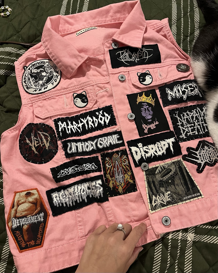 Photo of powder pink denim vest with assorted band patches sewn on it
