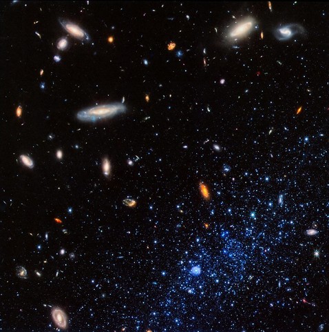 Image description from source link in toot: A concentration of bright blue stars occupies the bottom right corner of the image. At bottom center within them is a small blue bubble. The stars and bubble are part of a diffuse dwarf galaxy that extends beyond the image border. Background galaxies are scattered across the image, with some particularly prominent spirals located at upper left and upper right. The background of space is black.