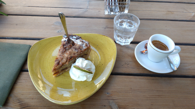 Dunkler Apfelkuchen mit Sahne (und einer gedörrten Limette in der Sahne), ein Glas Wasser und ein Espresso.