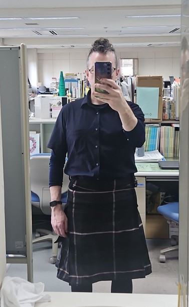 a photo of a man with a soft fauxhawk, dark blue shirt, and kilt with a black, grey, purple, red and white tartan