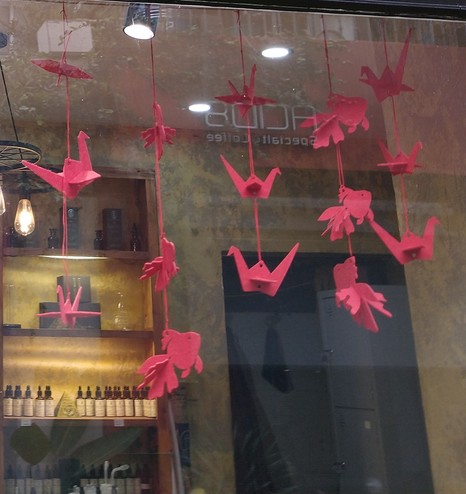 A photo of a cafe window decorated with what appear to be red origami fish and cranes suspended on strings.