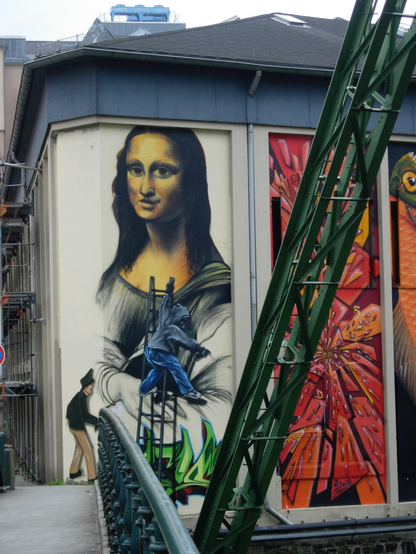 realistisches graffitti mit mona lisa, einem sprayer im hoodie der gerade das bild sprayt und einem polizisten, der den sprayer verhaften will … seitlich im vordergrund ein stützpfeiler der wuppertaler schwebebahn …