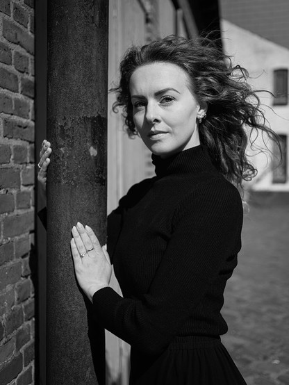 Frau, die sich an einer Straßenlaterne festhält und deren Haare durch den Wind verweht werden