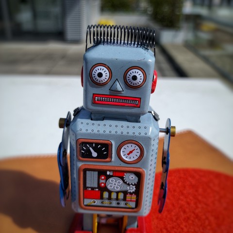 ein aufziehbarer Blech-Roboter wird von der Sonne beschienen — und hat einen leicht panischen Gesichtsausdruck, quasi genauso als wenn man wieder einen mehr als flachen Spruch auf diesem Account gepostet hat und hinterher feststellt: „Uiuiui, da war Humor drin, was hab ich mir dabei nur gedacht“