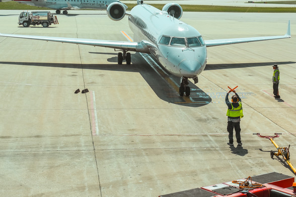 Airport ground crew signals to approaching commercial aircraft at gate.