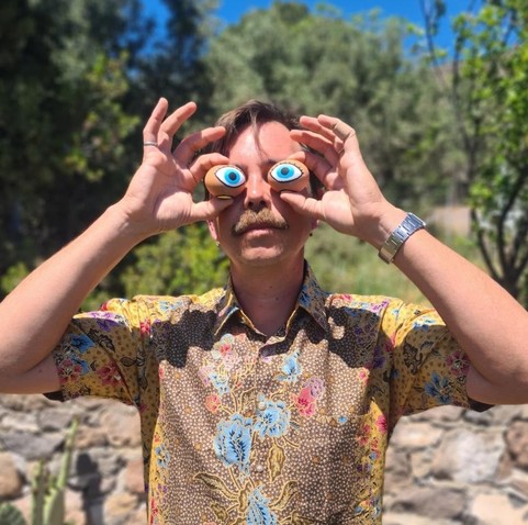 Artist James Bridle holds up traditional painted Easter eggs to his face, decorated with human, goat, and cuttlefish eyes.