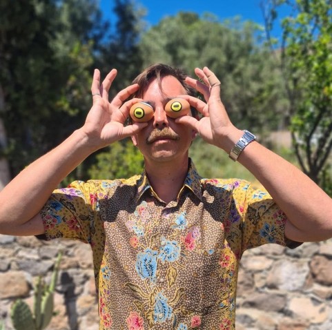 Artist James Bridle holds up traditional painted Easter eggs to his face, decorated with human, goat, and cuttlefish eyes.