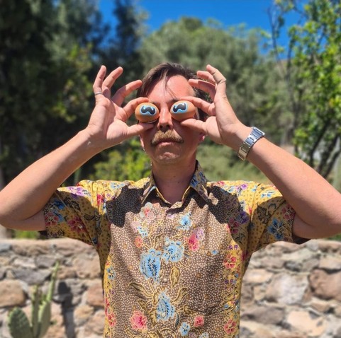 Artist James Bridle holds up traditional painted Easter eggs to his face, decorated with human, goat, and cuttlefish eyes.