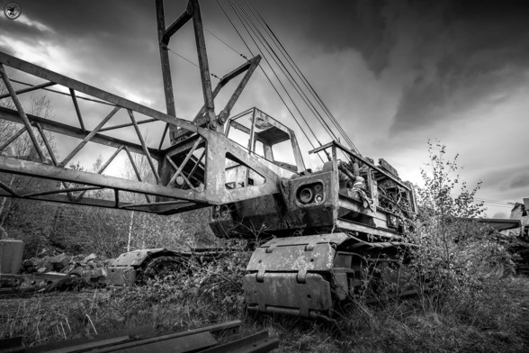 Monochrome shot of old mining crane sat in over grown weeds