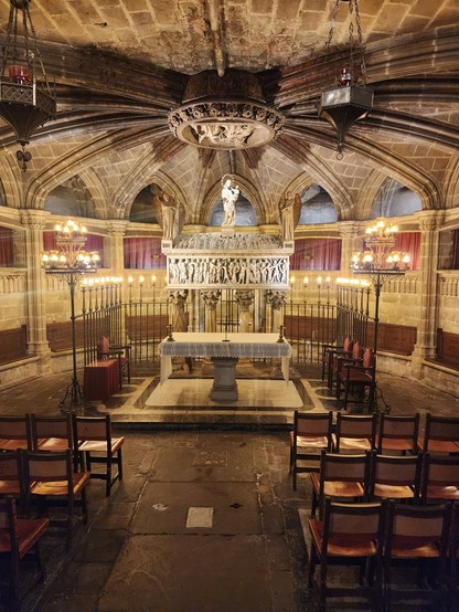 circular stone room about 6 meters in diameter with two sections of wooden chairs facing a stone altar, behind and above which is a stone reliquary casket carved in high relief. the ceiling is of ribbed vaulting that meets at the center.
