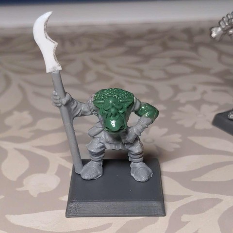 An in progress shot of a plastic model orc with various areas re-sculpted in epoxy putty with a sad face