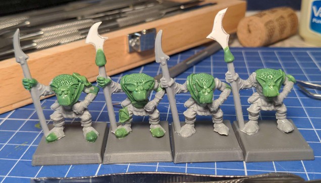 An in progress shot of four plastic model orcs with various areas re-sculpted in epoxy putty