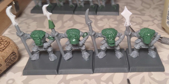 An in progress shot of four plastic model orcs with various areas re-sculpted in epoxy putty