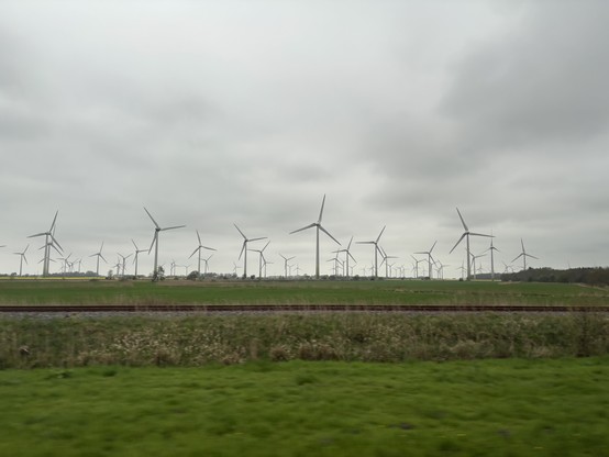 Ein Feld voller Windkraftanlagen, davor eine alte Bahntrasse