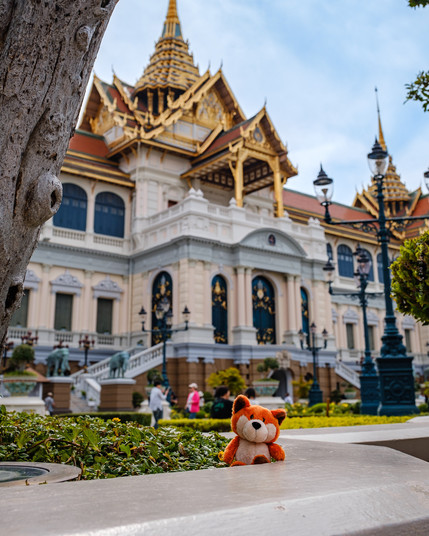 Ein Plüschfuchs sitzt vor einem reichlich verzierten Palastgebäude im Königspalast in Bangkok, Thailand.