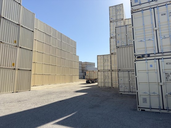 A photograph of a lot full of empty shipping containers, stacked atop each other 6 deep. A truck maneuvers between the stacks.