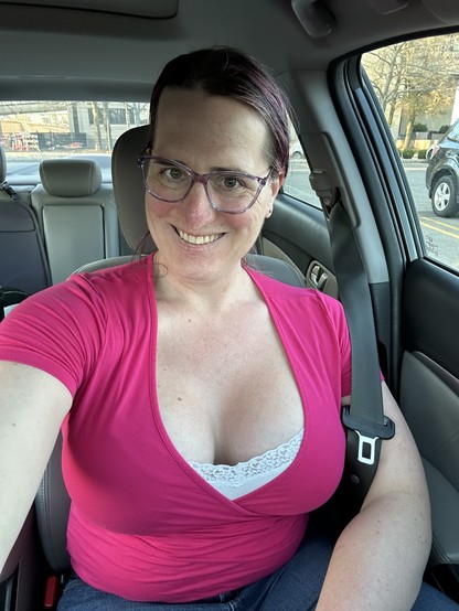 Selfie of a lady with purple hair and a red blouse sitting in a car.