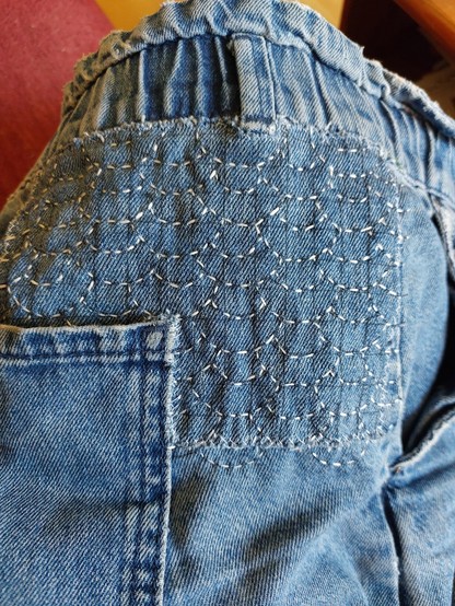 Flicken in Sashiko-Technik auf einer Jeans. Der Flicken zieht sich oben und an der Seite um die rechte Gesäßtasche. Die Stickerei ist mit hellem Stickgarn ausgeführt und zeigt ein Schuppenmuster.