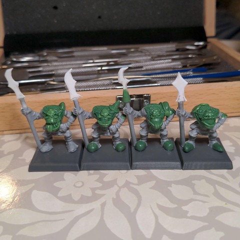 An in progress shot of four plastic model orcs with various areas re-sculpted in epoxy putty