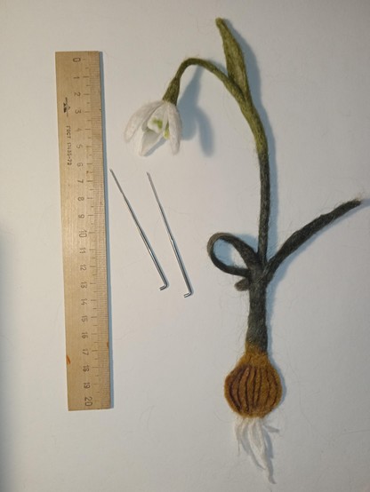 On a white background near the line lies a snowdrop, as if it were being pulled out of the ground. This is a bookmark with a picture of plants, made of nettle with needle felting. Next to the snowdrop, leave two special toys for felting. Thank you for your attention!