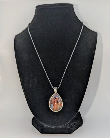 A teardrop-shaped pendant necklace displayed on a black jewelry mannequin. The setting is silver and the design is primarily orange and ultramarine blue.