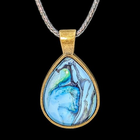 A close-up of a teardrop-shaped pendant. The setting is bronze and the design is primarily light blue.