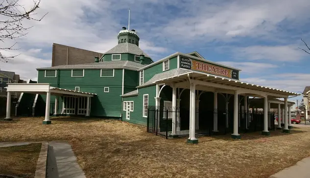 The image shows a historic building that appears to be a theater, characterized by its green exterior and round architectural features. It has a prominent entrance with the word "THEATRE" displayed on the front. Surrounding the building are grassy areas and trees, and the sky is partly cloudy. The design suggests a unique and possibly vintage style, indicating it may hold some historical significance.

Image Credits: Wikimedia / Hustvedt / CC BY-SA 3.0