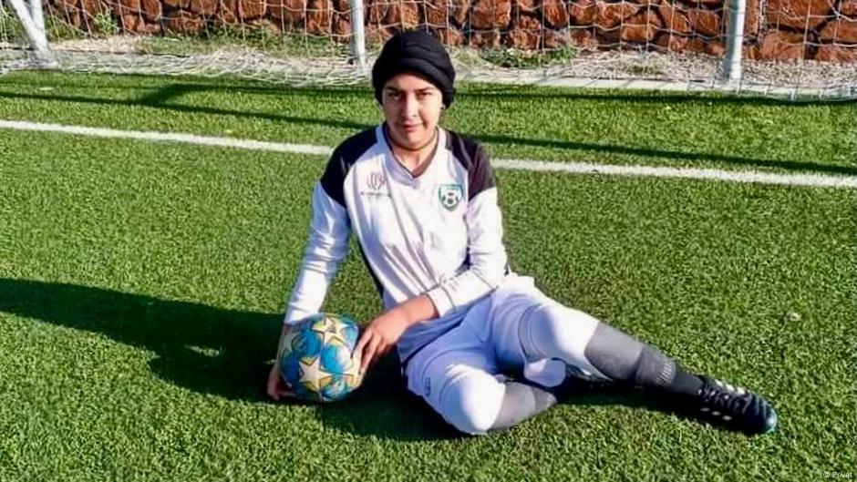Torhüterin Nazira Khairzad sitzt auf dem Rasen vor einem Fußballtor und halt einen Ball in ihren Händen
