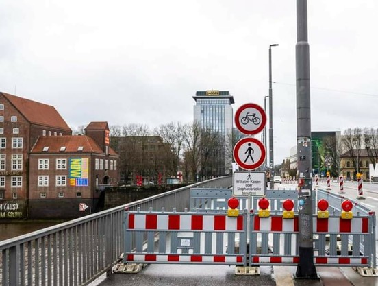 Gesperrter Fuß- und Radweg mit Verweis auf einen Umweg von mehreren Kilometern über Stephanibrücke oder Wilhelm-Kaisen-Brücke. Von den zwei parallel verlaufenden Autospuren in beide Richtungen ist eine gesperrt worden. Der Radverkehr nutzt die Autofahrbahn mit.
Die Straßenbahngleise zwischen den Autospuren mittig der Straße sind frei.