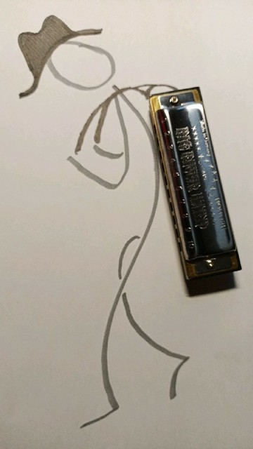 Scribble of stickperson with a hat, carrying a small G blues harp on its back. (Harp lies on the paper.)