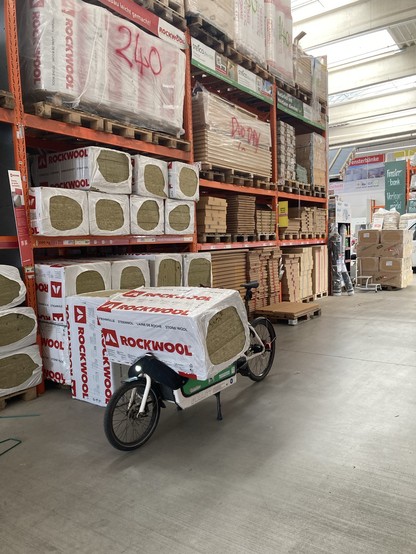 Foto zeigt Lastenrad im Baumarkt mit einer großen Packung Dämmwolle beladen. 