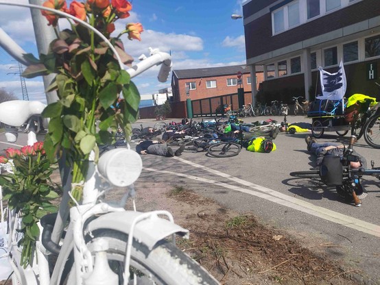 Menschen und Fahrräder liegen auf einer Straße, im Vorderung ein weißes Fahrrad, ein Ghostbike