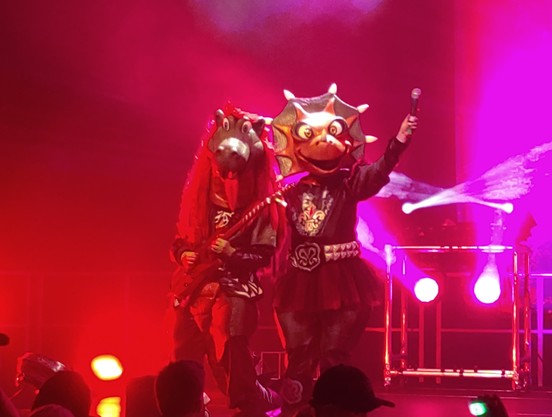 2 Musiker in Dino-Kostümen (RiffiRaffi und MilliPilli) der Kinder-Metal-Band HeavySaurus bei einem Live-Auftrit auf der Bühne in der Leuphana Uni Lüneburg.
