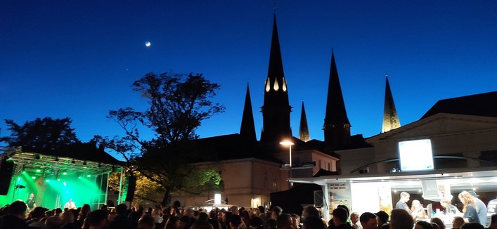 Rock gegen Rechts auf dem Schlossplatz in Oldenburg. Links die Bühne in grünem Licht, mittig im Hintergrund die Lambertikirche, am dunklen Himmel der zunehmende Mond.