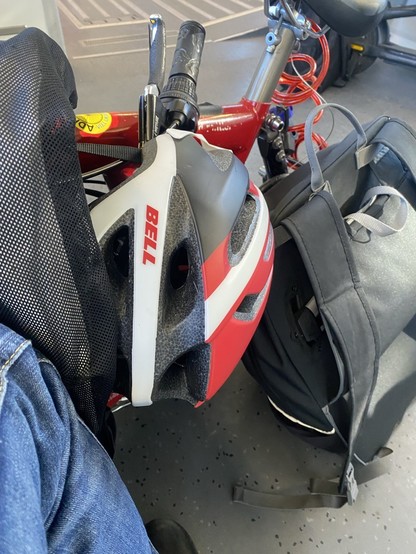 Auf dem Boden (eines Regionalzuges)ein Kuddelmuddel aus einem Bein, einem Faltrad, einen Fahrradhelm, einem Rucksack. Darüber noch ein Anorak.