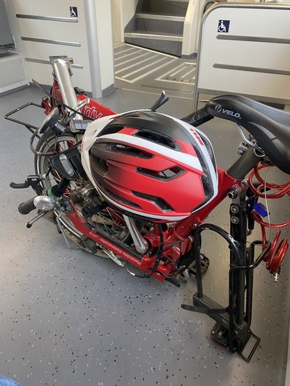 mein Faltrad im leeren Zug auf dem Boden. Es handelt sich um ein rotes Birdy von 2000, an dem Fahrrad hängt ein rot-weißer Fahrradhelm.