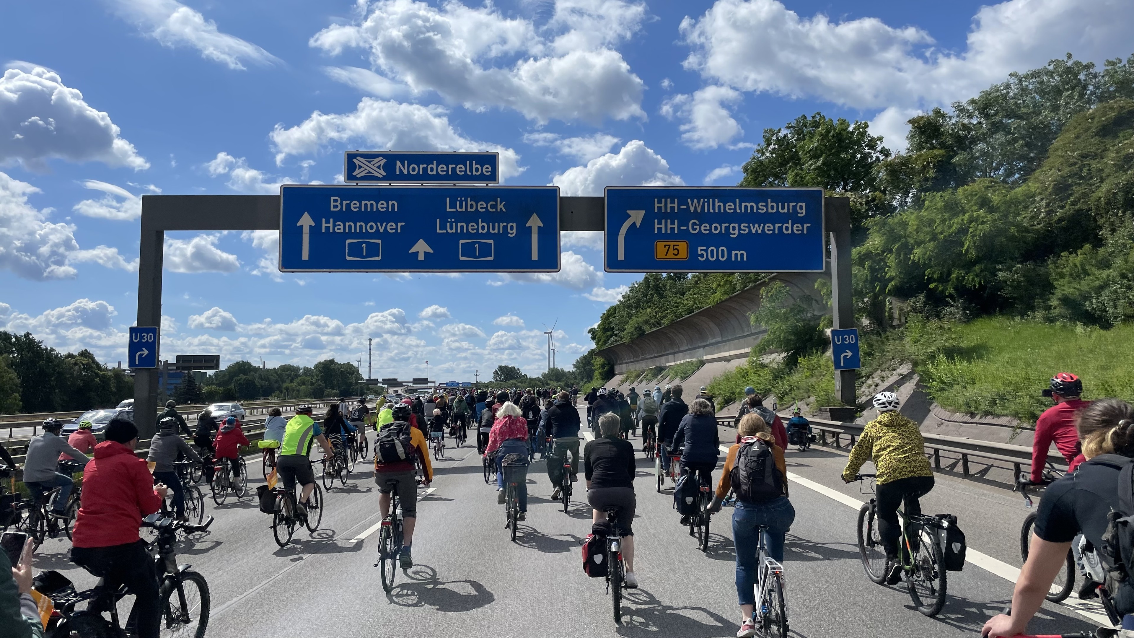Sehr viele Fahrradfahrer auf der Autobahn unter dem blauen Schild zur Ankündigung des AB-Kreuzes Norderelbe, rechts gehts in 500m ab nach HH-Wilhelmsburg.