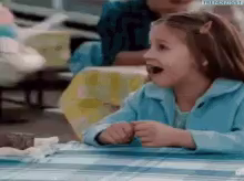 a little girl sitting at a table with her mouth open