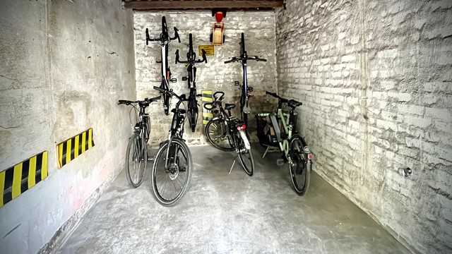 In einer Garage hängen vier Fahrräder an den Wand. Vier weitere sind dazwischen auf den Boden gestellt. 

Es wird mit der hintere Teil der Garage genutzt.