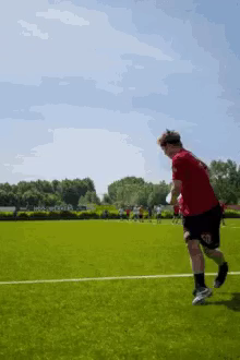 a man in a red shirt and black shorts is running on a field