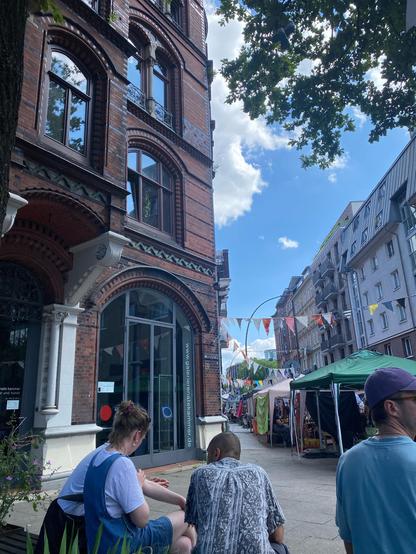 Alte und neue Gebäude im Münzviertel. Die Blätter eines Baumes, blauer Himmel mit Wattewolken, Wimpelketten, Menschen, Stände.