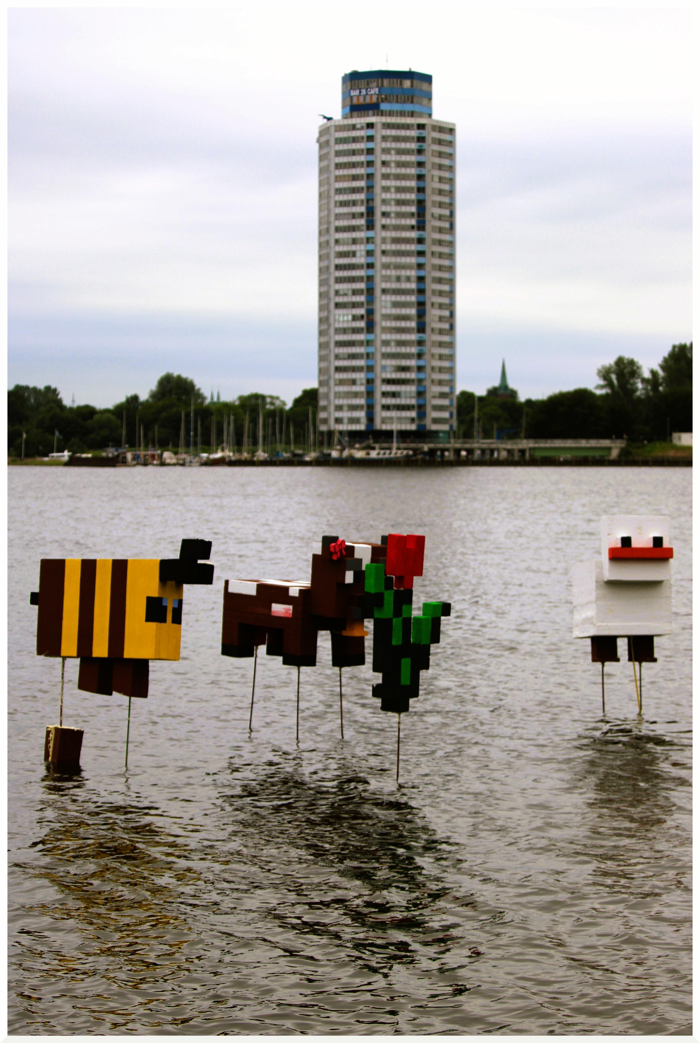 Mehrere Minecraft-Figuren im Wasser der Schlei: eine Biene, eine Kuh, eine Ente und eine Blume. Auf Stahlstäben befestigt, schweben die Figuren über der Wasseroberfläche. Im Hintergrund der Wikingturm, wahrlich kein herausragender Vertreter des Kubismus. Mehrere Minecraft-Figuren im Wasser der Schlei: eine Biene, eine Kuh, eine Ente und eine Blume. Auf Stahlstäben befestigt, schweben die Figuren über der Wasseroberfläche. Im Hintergrund der Wikingturm, wahrlich kein herausragender Vertreter des Kubismus.
