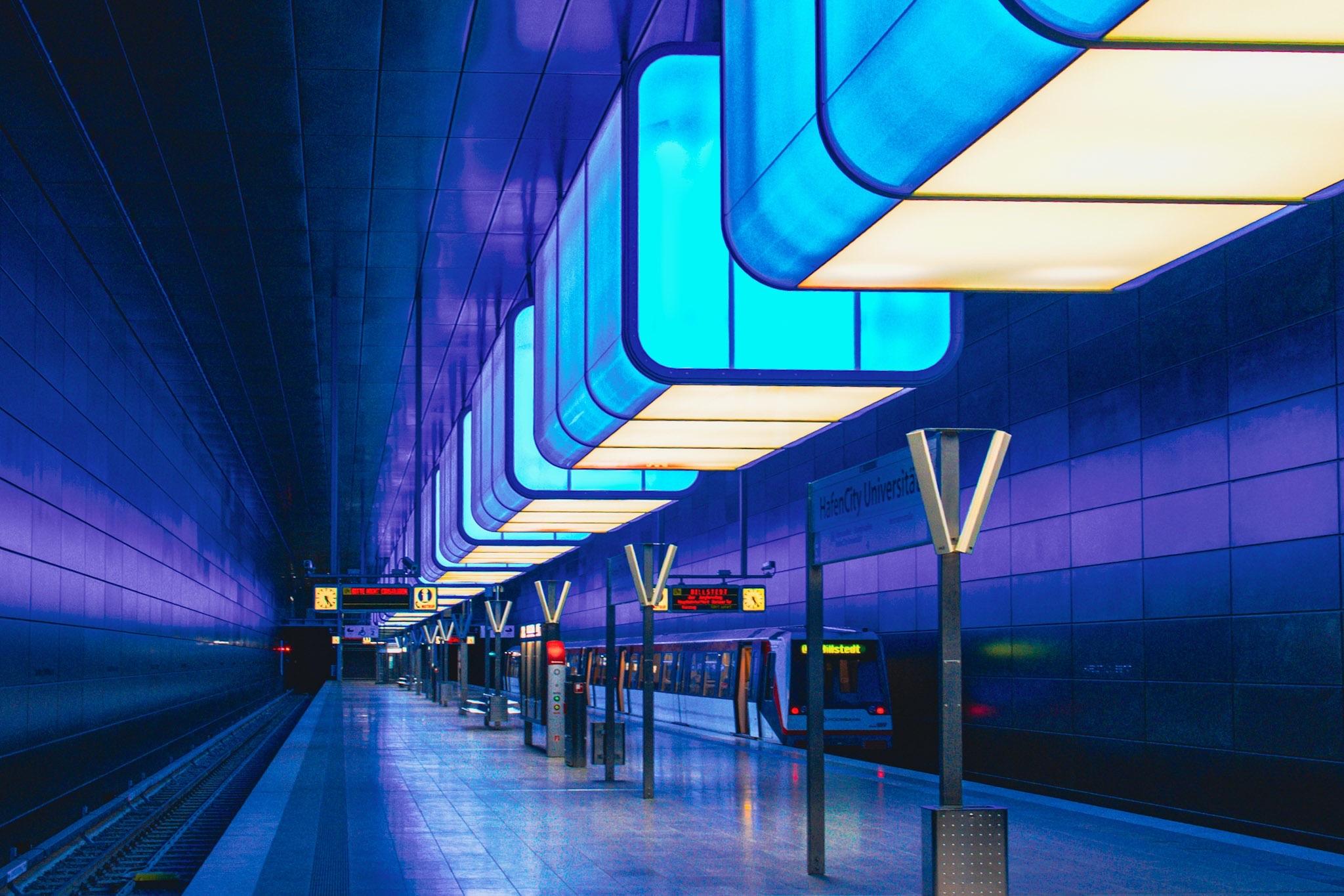 Eine beleuchtete U-Bahn-Station mit modernen Designelementen und einer blauen und violetten Farbpalette. Es gibt Oberlichter, Bahnsteige mit Bänken, Beschilderung und einen am Bahnhof wartenden Zug. Eine beleuchtete U-Bahn-Station mit modernen Designelementen und einer blauen und violetten Farbpalette. Es gibt Oberlichter, Bahnsteige mit Bänken, Beschilderung und einen am Bahnhof wartenden Zug.