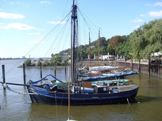 Kleine historische Segelschiffe in einem Hafen, im Hintergrund ein bewaldet Hang.