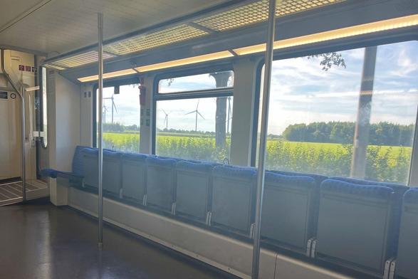 Blick aus dem Fahrradabteil im RE7 auf eine grüne Wiese mit Windrädern und einem Waldstück