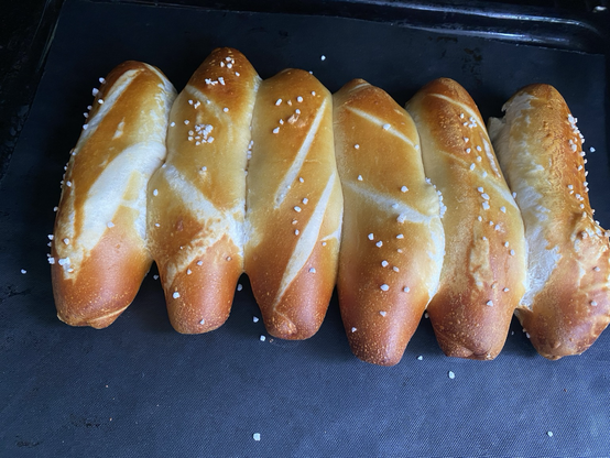 sechs Aufback-Laugenstangen, die zu einem einzigen großen Fladen zusammen gebacken sind. Man sieht aber noch, wo man sie durchbrechen kann. Ich hätte sie mit mehr Abstand aufs Blech legen müssen.