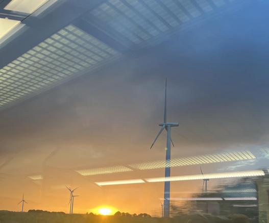 Windräder im Sonnenuntergang. Die Lichter aus dem Zug reflektieren im Zugfenster