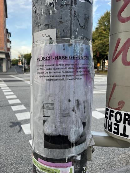 A street pole with a poster in German announcing a found plush rabbit. The poster includes a message from Michelle Boschette, describing the rabbit's last known location and requesting anyone with information to contact her via email. The surrounding area appears urban.